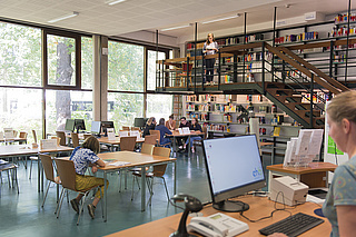 Großer Lesesaal mit Arbeitsplätzen, Empore, Bücherregalen und Ausleihtheke