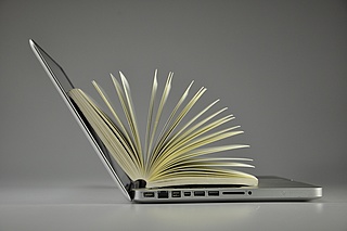 Laptop mit aufgeschlagenem Buch