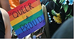 Personen tragen eine Regenbogenfahne mit Aufschrift Queer & Proud
