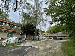 Baustelle mit Materialien und einem Bauzaun der vor einem länglichen Gebäude steht