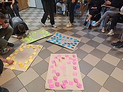 Vier Plakate beklebt jeweils mit grünen, gelben, blauen und rosa Post-Its liegen auf einem Steinboden  