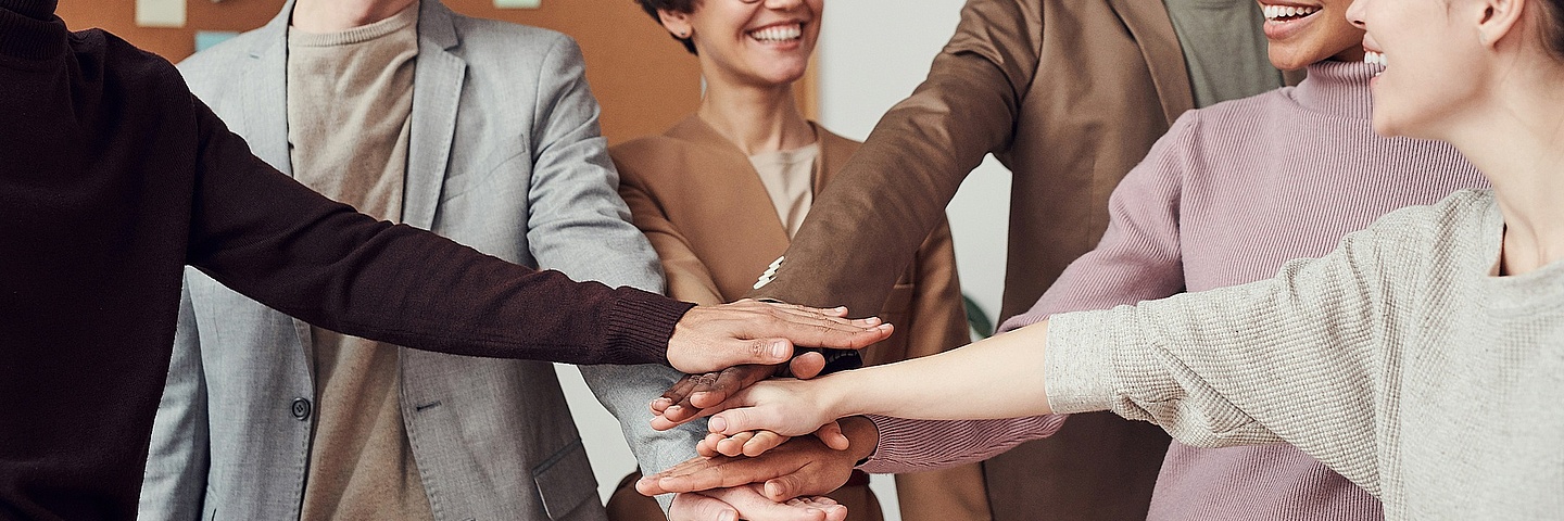 Personengruppe im Kreis bildet mit aufeinanderliegenden Händen einen Turm