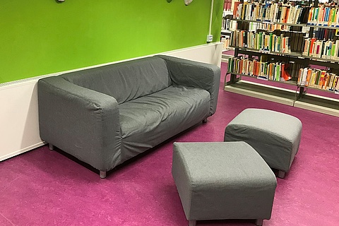 Ein Sofa und zwei Hocker neben Regalen