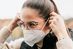 Frau mit Brille zieht sich FFP 2 Maske aüber
